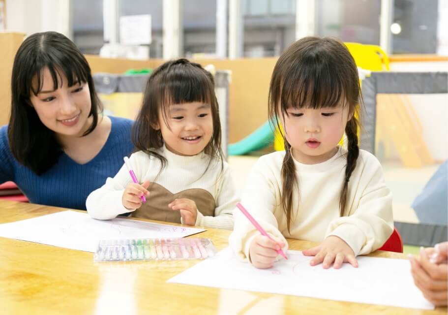 絵を描く子供と見守る先生の画像